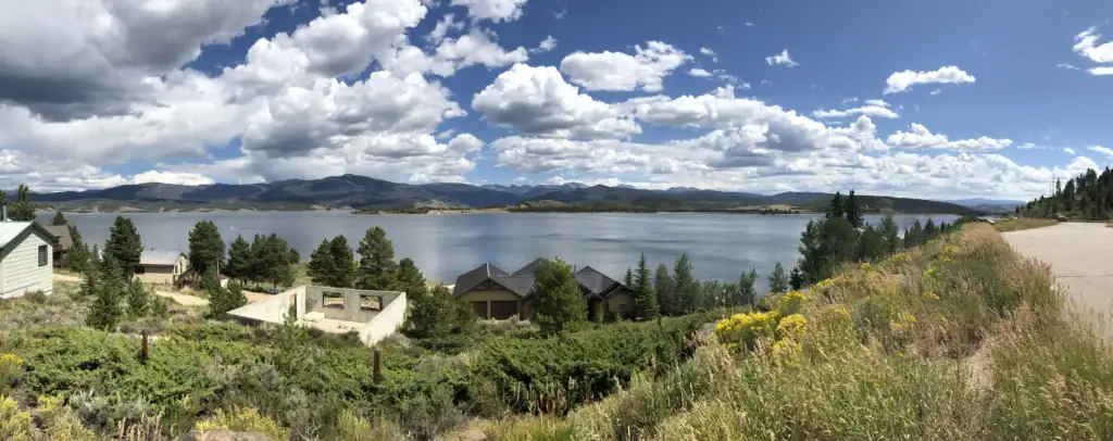 A panoramic view of a mountain lake in Colorado with dry vegetation and brush along the hillside, illustrating the natural landscapes vulnerable to what causes wildfires in Colorado.