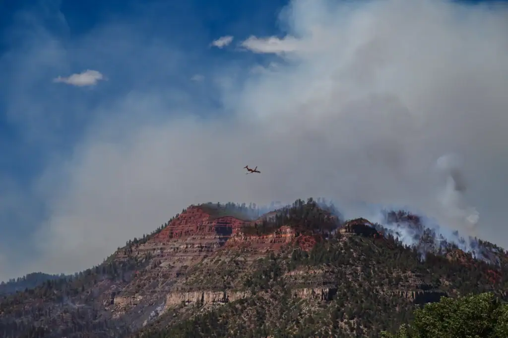 An active firefighting plane flying over a rugged mountain ridge, providing critical help during a Colorado wildfire as thick smoke billows from the trees.