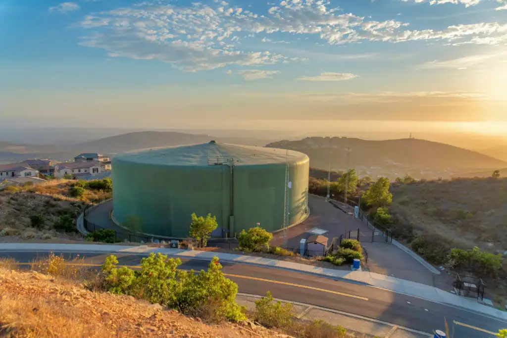 A large municipal water storage tank on a hilltop near a suburban WUI neighborhood, representing municipal water infrastructure and pressure systems.