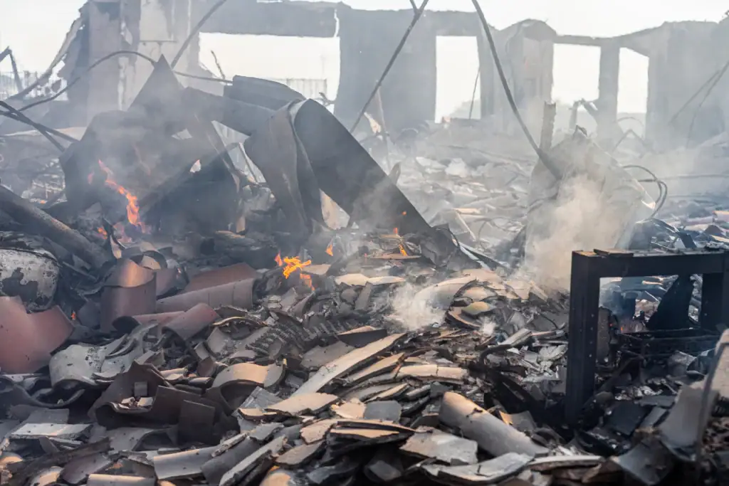 A destroyed building smoldering after a wildfire, representing structural damage that drains municipal water supply pressure.