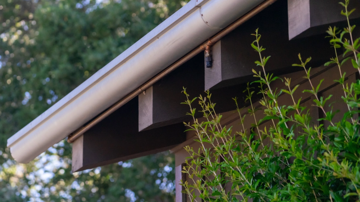 A close-up view of roof eaves and a gutter with a Frontline wildfire defense system nozzle mounted underneath.