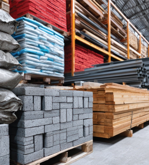 Stacked lumber, concrete paver blocks, and construction materials stored inside a hardware supply warehouse.