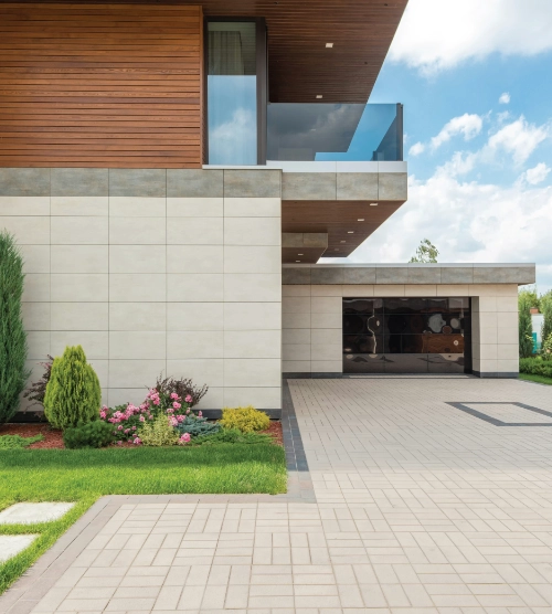 Modern residential property featuring a paved stone driveway, manicured lawn, and attached garage.