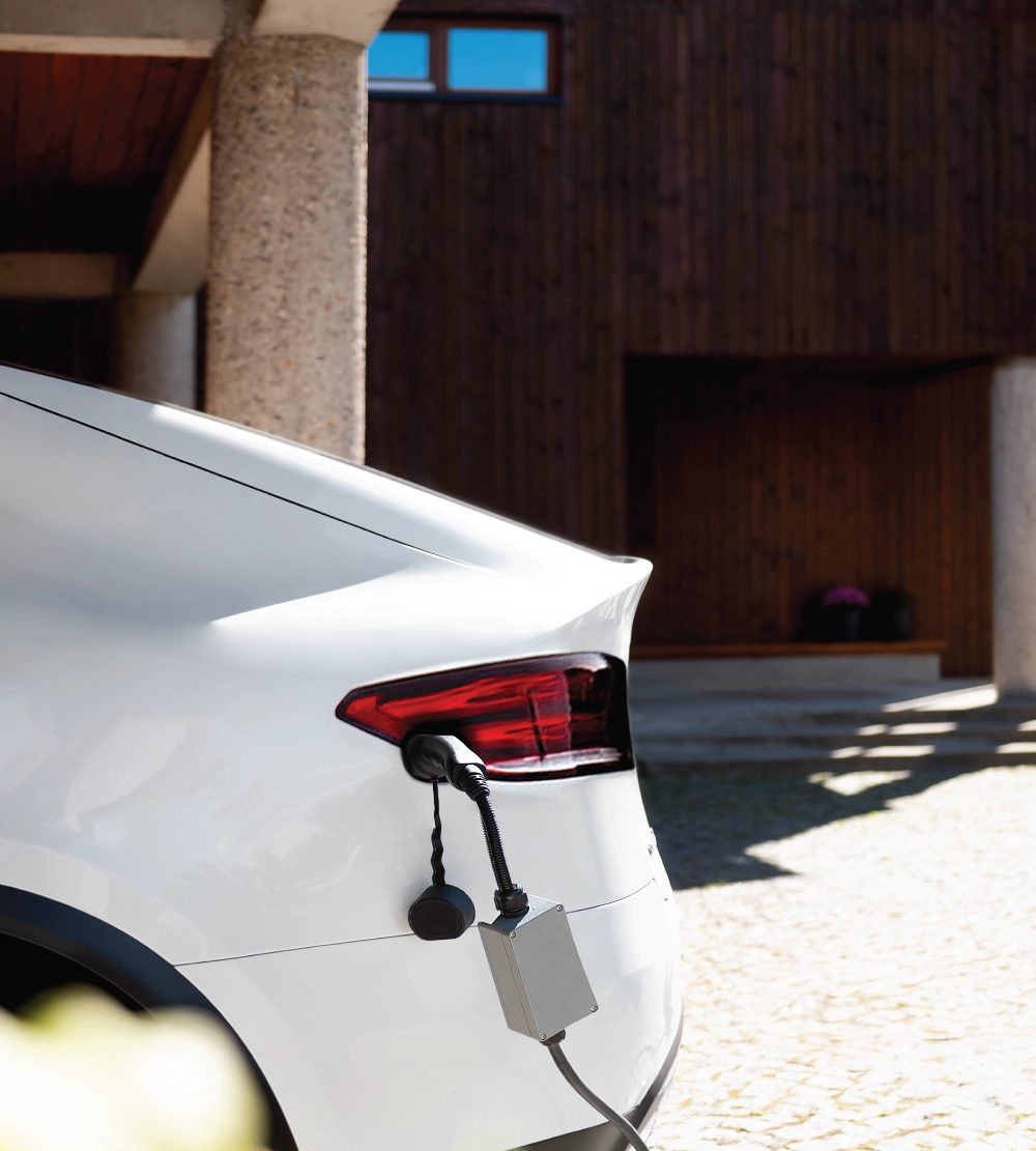 Rear view of a white electric vehicle plugged into an outdoor charger parked outside a modern home.