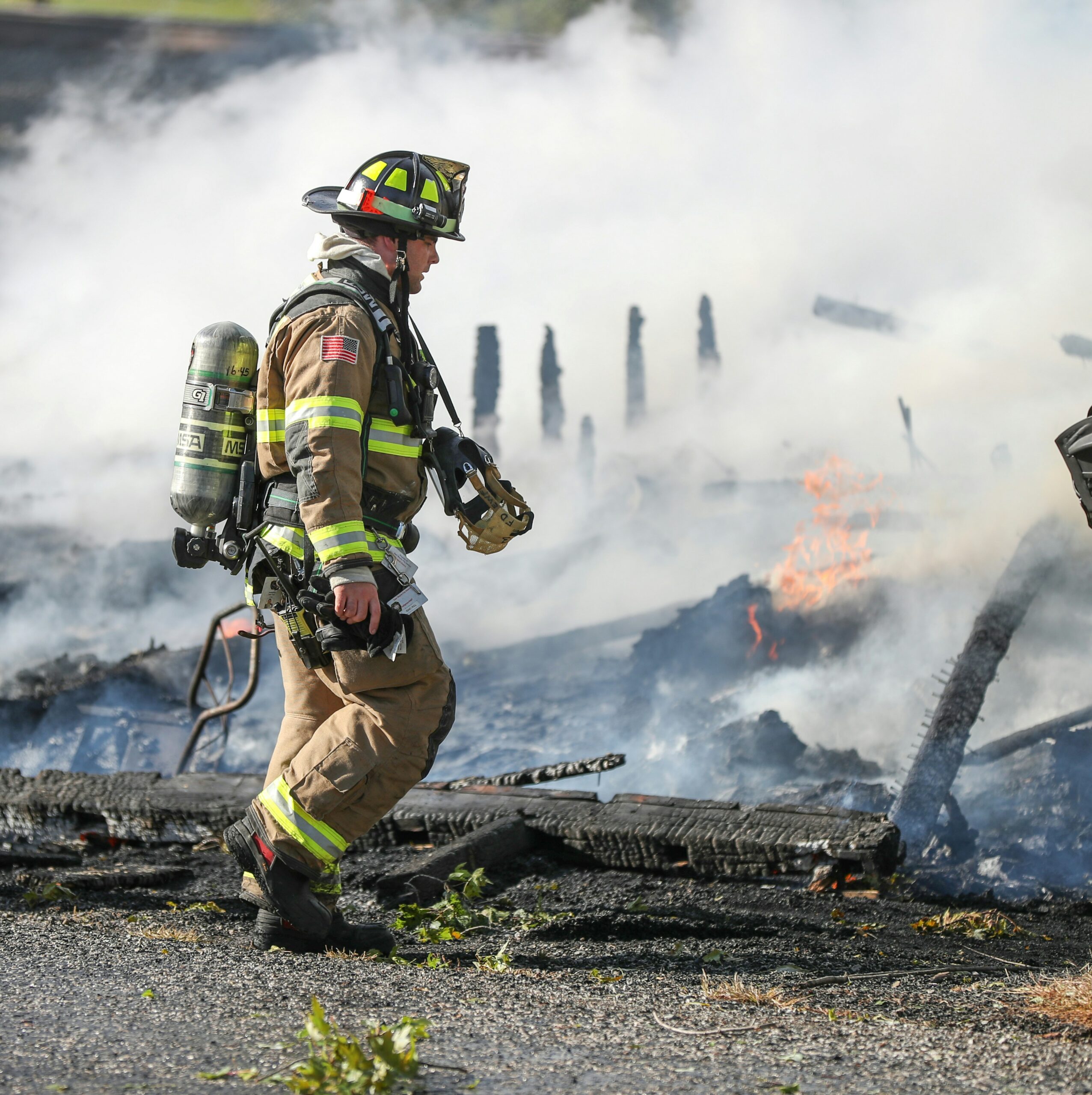 Firefighter at the scene of a structure fire as smoke rises from burning debris.